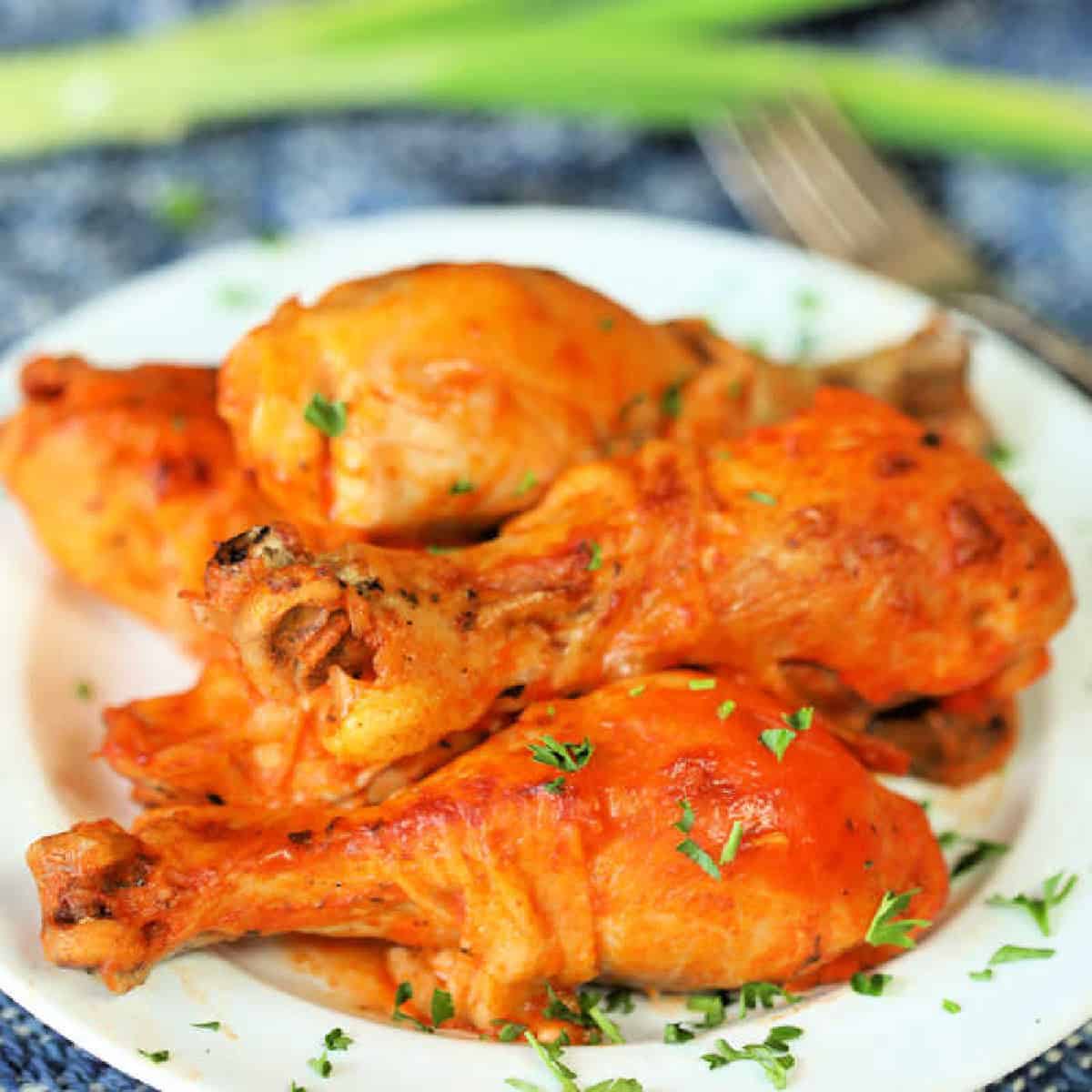 Close up image of buffalo chicken drumsticks on a white plate. 