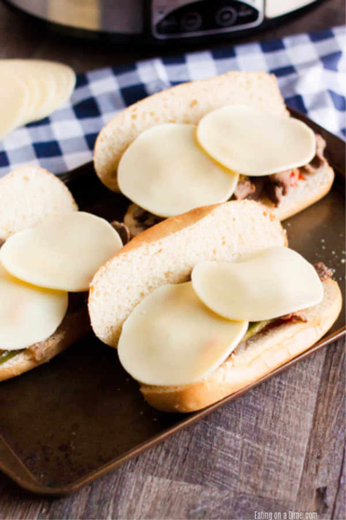 Philly cheesesteaks sandwiches on a baking sheet with slices of cheese. 