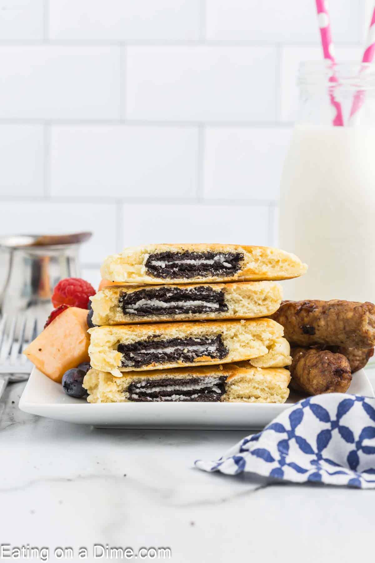 Oreo Pancakes stacked cut in half so you can see the Oreo cookies in the pancakes with a side of sausage links and fresh fruit
