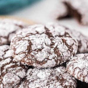 Close-up of chocolate crinkle cookies dusted with powdered sugar, stacked slightly on top of each other like decadent brownie cookies, showcasing their distinctive cracked surface.