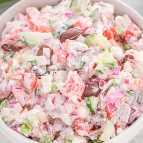 An easy Greek salad recipe featuring a colorful bowl of diced cucumbers, tomatoes, red onions, black olives, and feta cheese, all mixed with a creamy dressing.