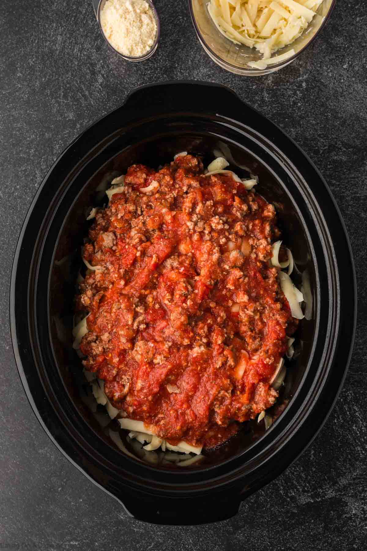 Ground beef mixture layered over shredded cheese in the slow cooker