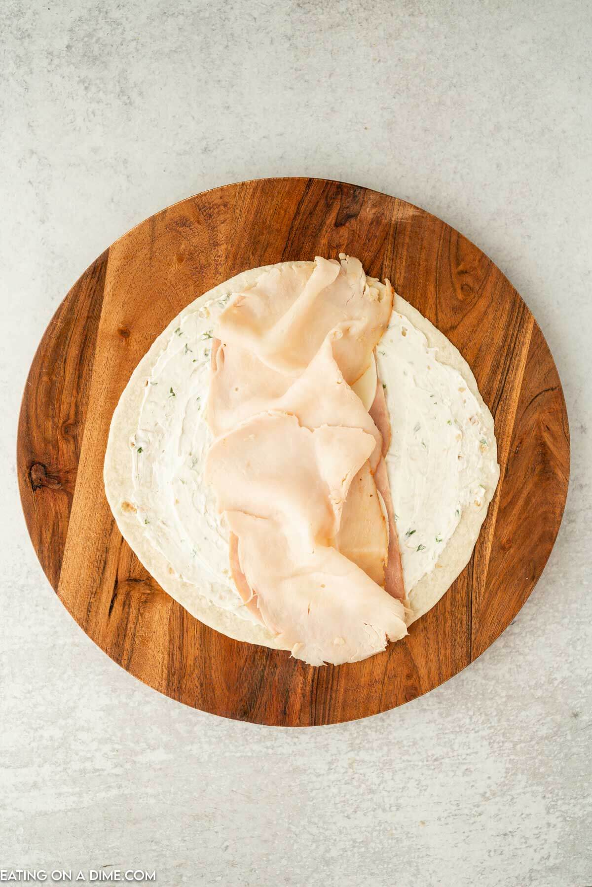 Tortilla with cream cheese spread and turkey and ham on a brown platter