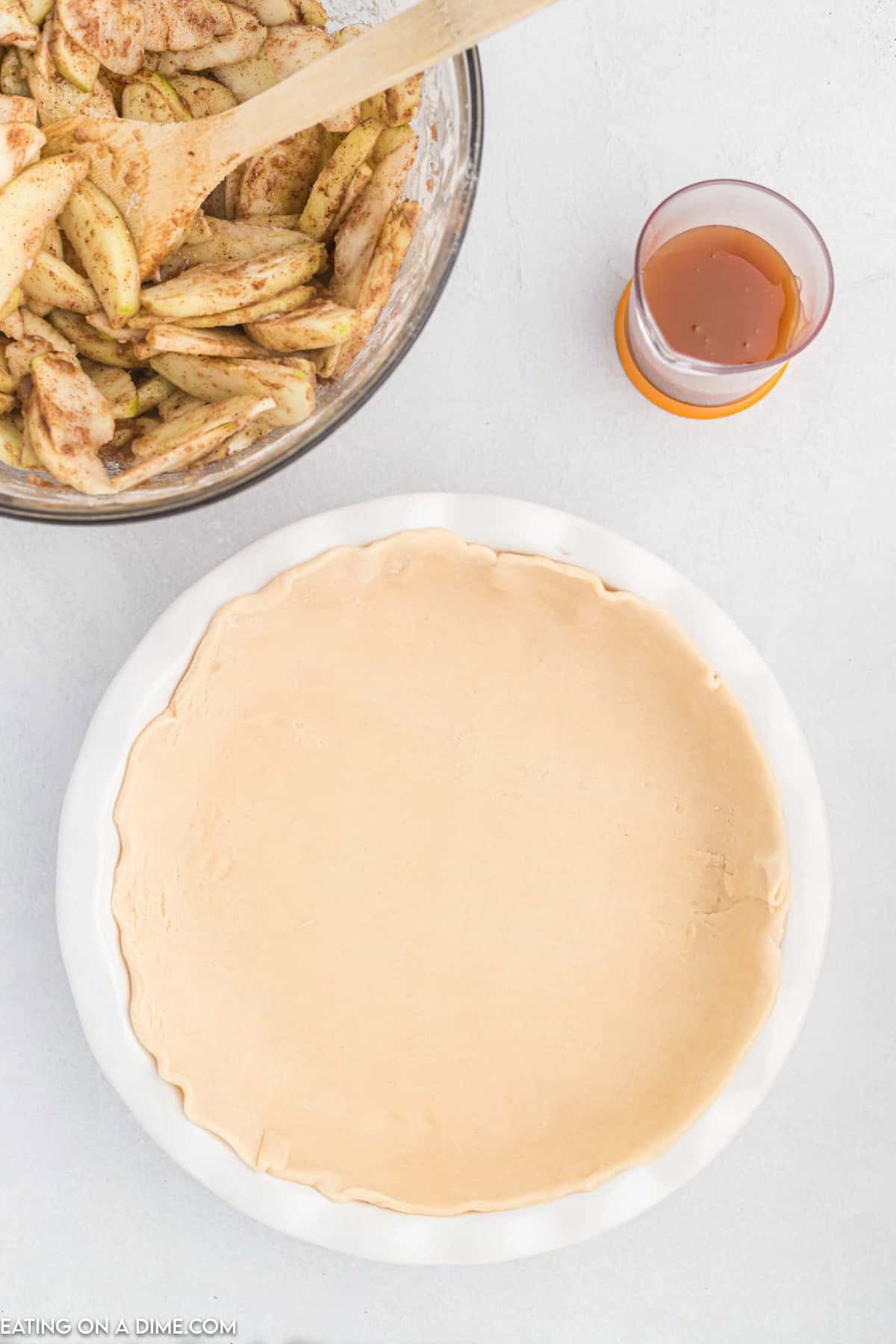 Pie crust pressed into a pie plate with a bowl of seasoned covered slice apples