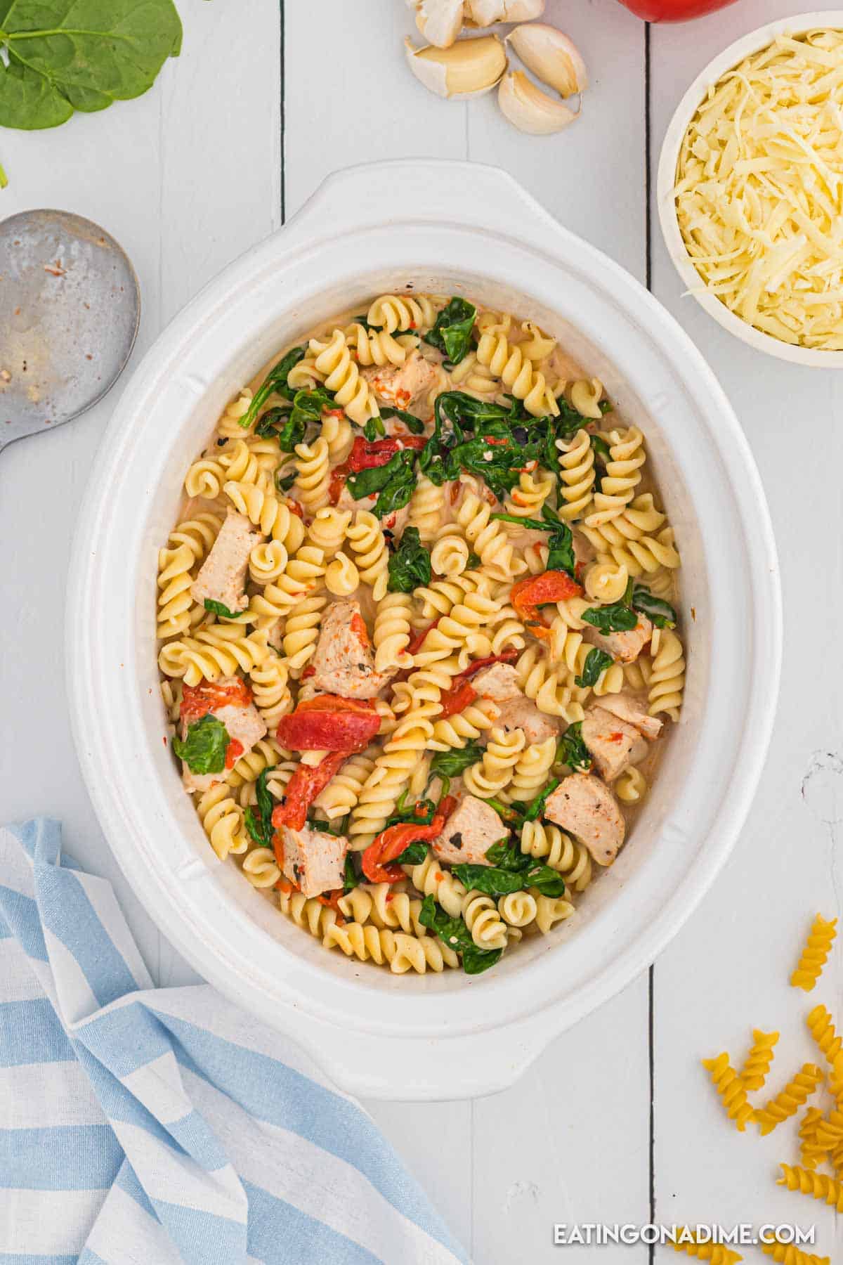 Adding pasta to the slow cooker with the cooked spinach, roasted peppers and chicken