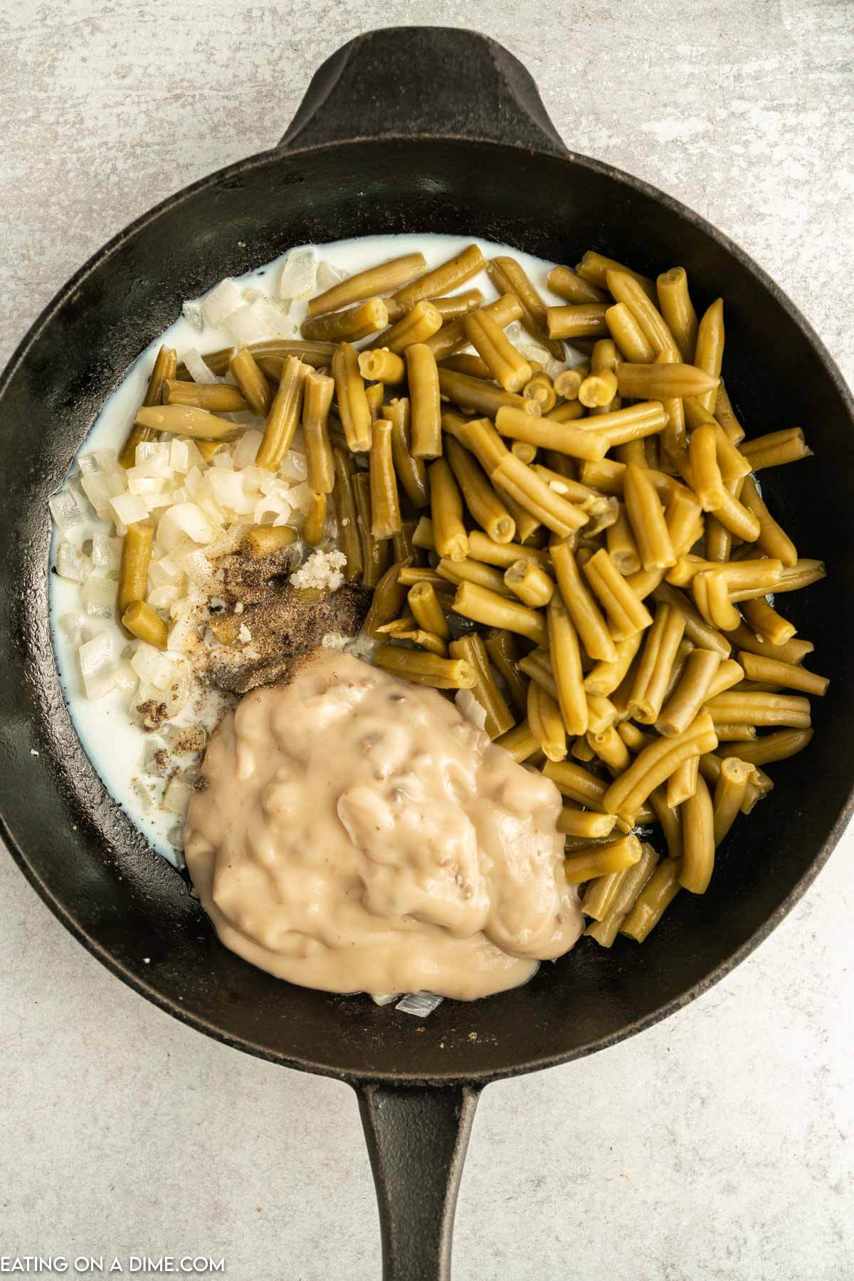 Green beans, cream of mushroom soup, milk, and seasoning combined in a cast iron skillet