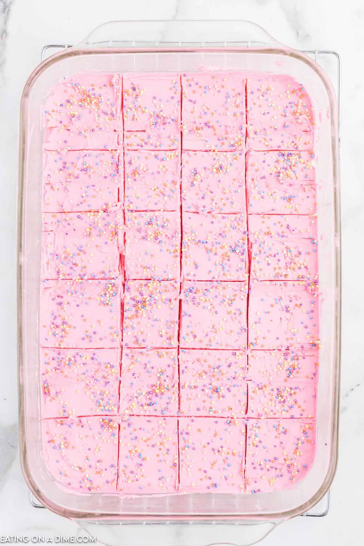 Sugar cookie bars in a baking dish topped with pink frosting with sprinkles