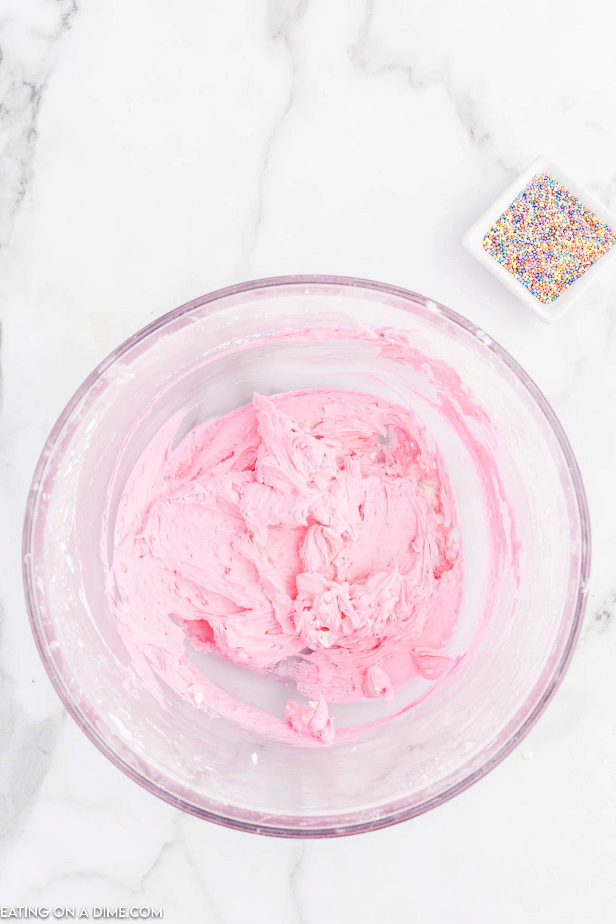 Pink frosting in a bowl with a small bowl of sprinkles on the side