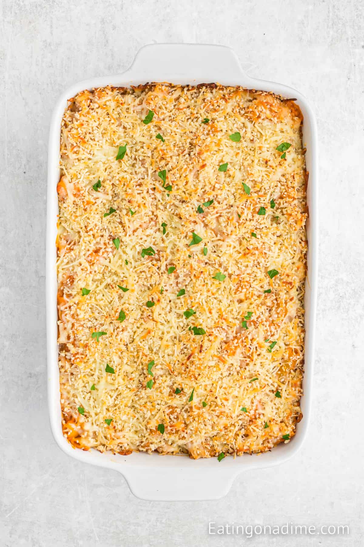 A delicious baked Olive Garden 5 Cheese Ziti casserole topped with melted cheese and sprinkled with chopped herbs, all elegantly presented in a rectangular white dish against a light gray background.