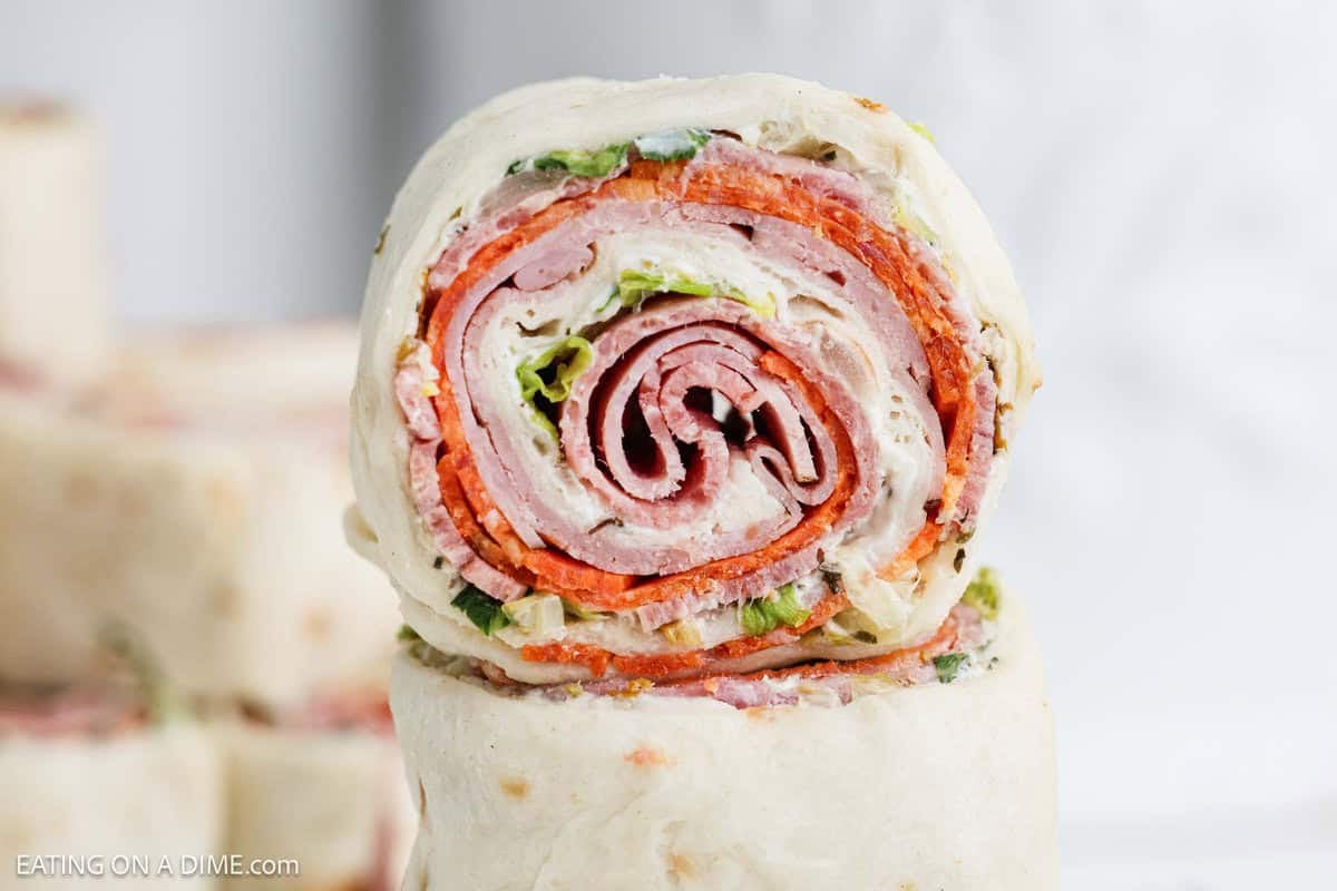 A close-up of pinwheel sandwiches showcases layers of turkey, pepperoni, lettuce, and cream cheese elegantly wrapped in a tortilla. Each slice reveals the vibrant spiral pattern of the ingredients.