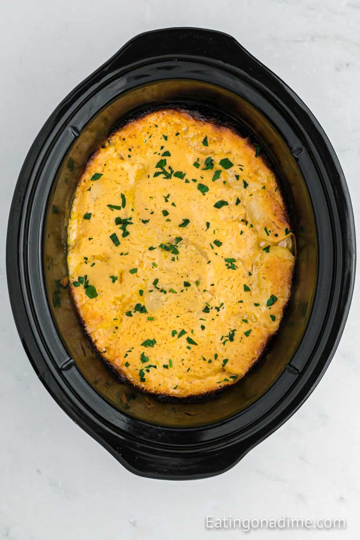 Cooked Au Gratin Potatoes topped with golden brown cheese in the slow cooker