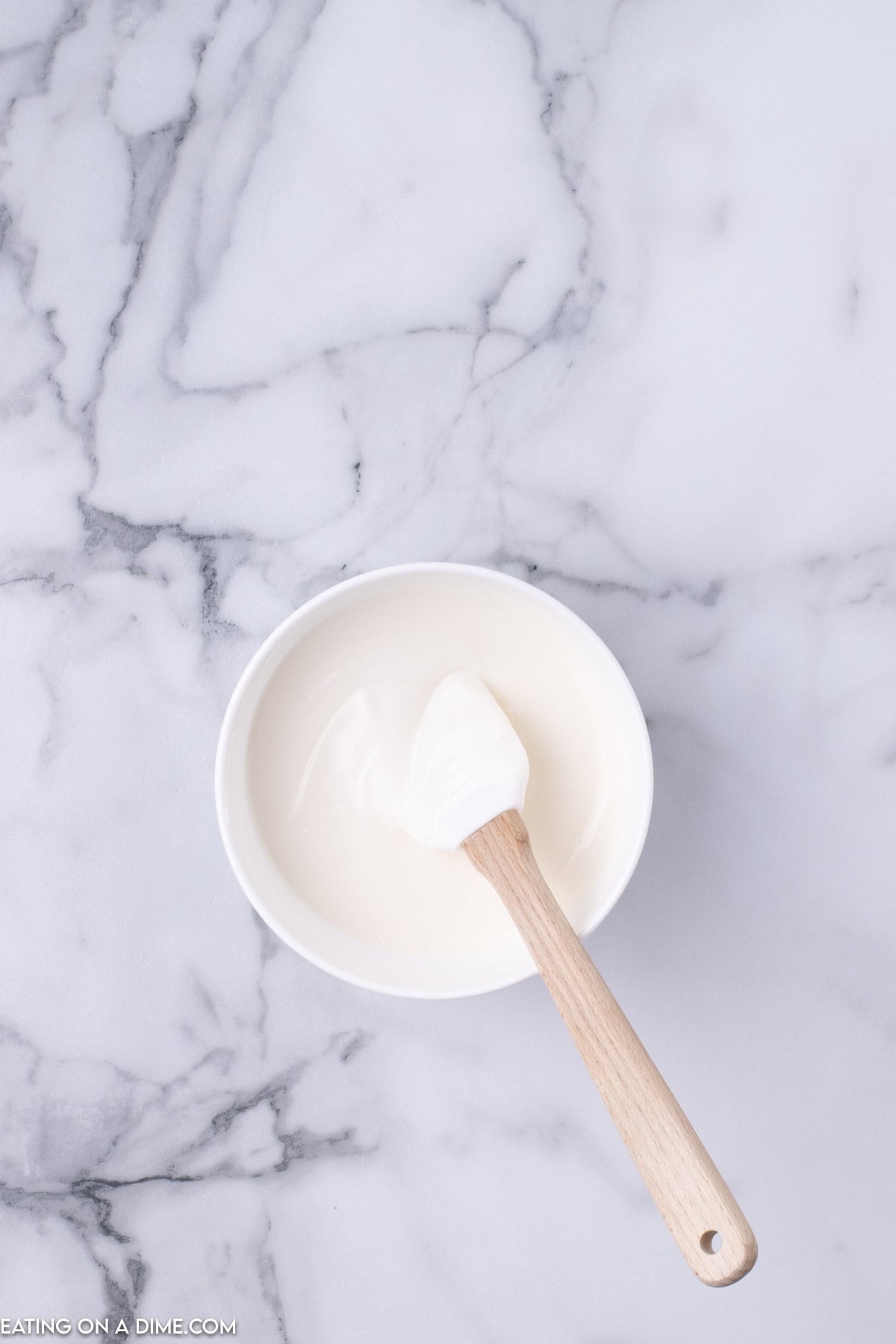 A white bowl filled with creamy white yogurt, placed on a marble countertop. A wooden spoon with a bit of yogurt on it rests inside the bowl, angled slightly to the side, evoking the cozy charm of Christmas Crunch mornings.