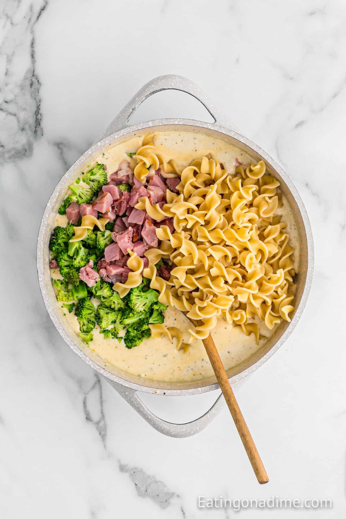 Egg noodles, diced ham and chopped broccoli added to the creamy mixture in a saucepan with a wooden spoon