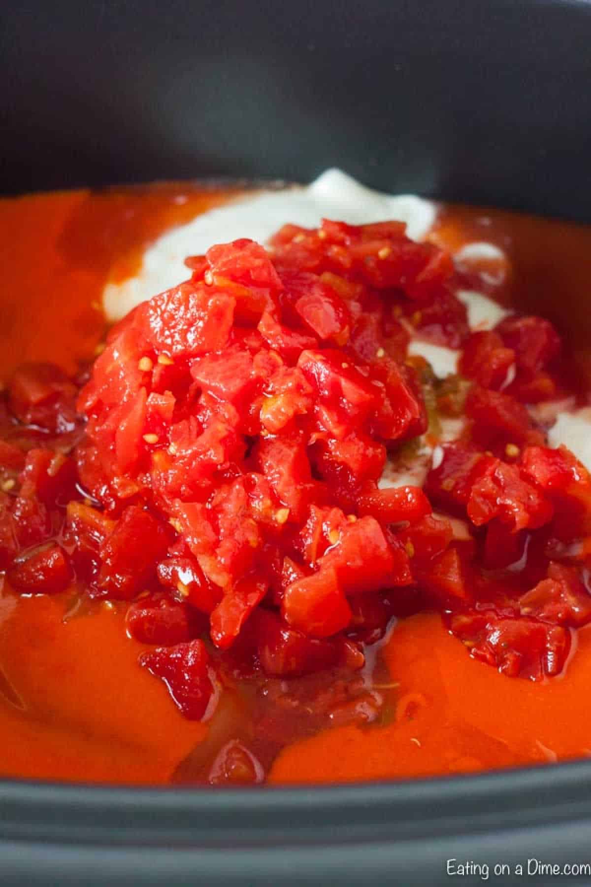 Chopped tomatoes sit on a bed of creamy sauce in a pot, reminiscent of a crock pot buffalo chicken enchilada casserole, with red marinade surrounding them. The vibrant colors suggest a preparation in progress, ready for cooking.