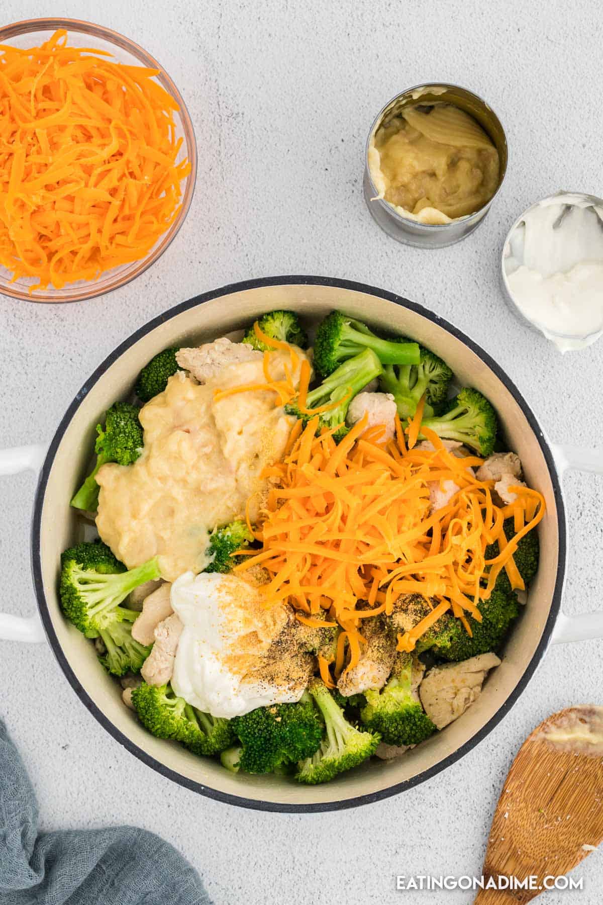 Cooked chicken in a large pot with broccoli, shredded cheese, sour cream and cream of chicken soup