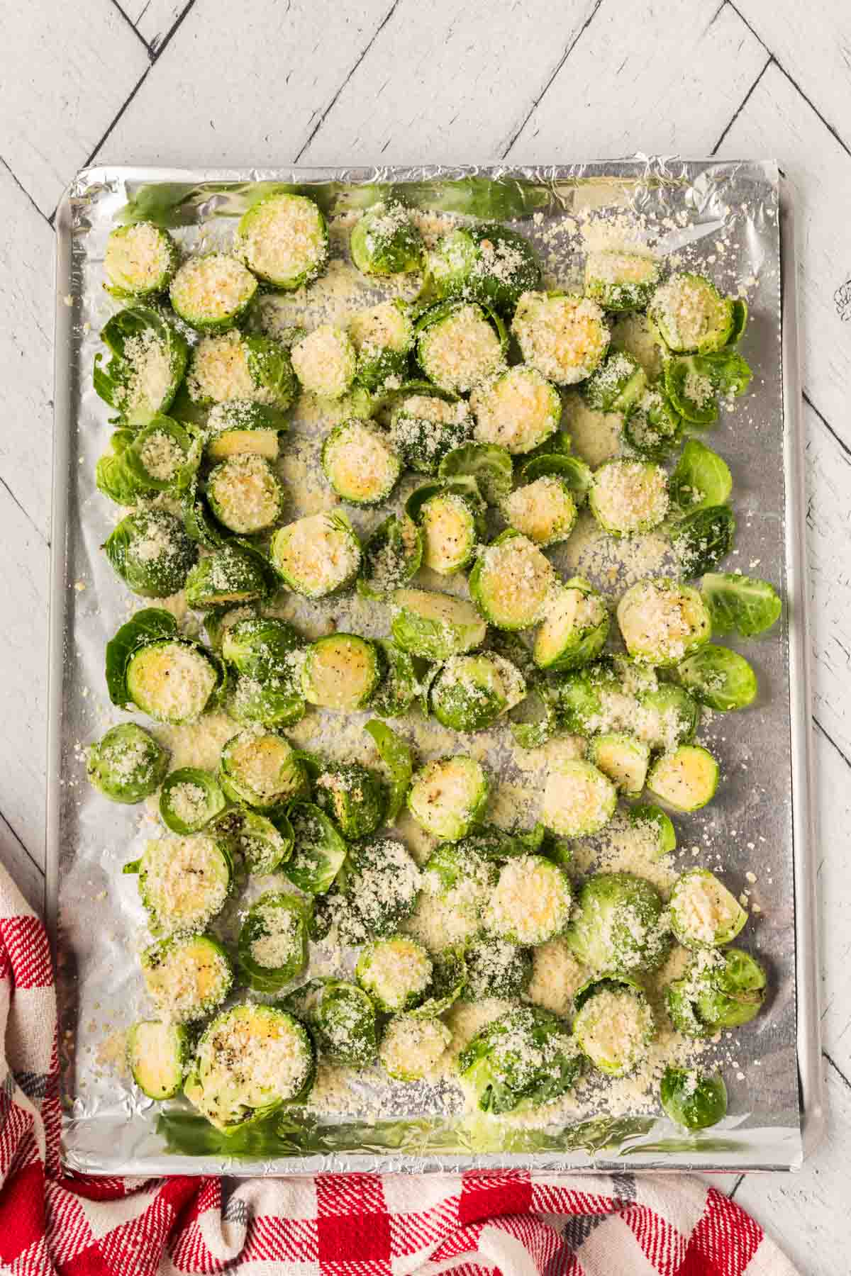 Brussel Sprouts spread on a baking sheet lined with foil topped with parmesan cheese