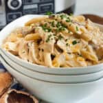 A bowl brimming with creamy pasta topped with chopped parsley. This dish combines penne and mushrooms in a light cream sauce, hinting at the richness of a slow cooker cheesy chicken penne waiting in the background.