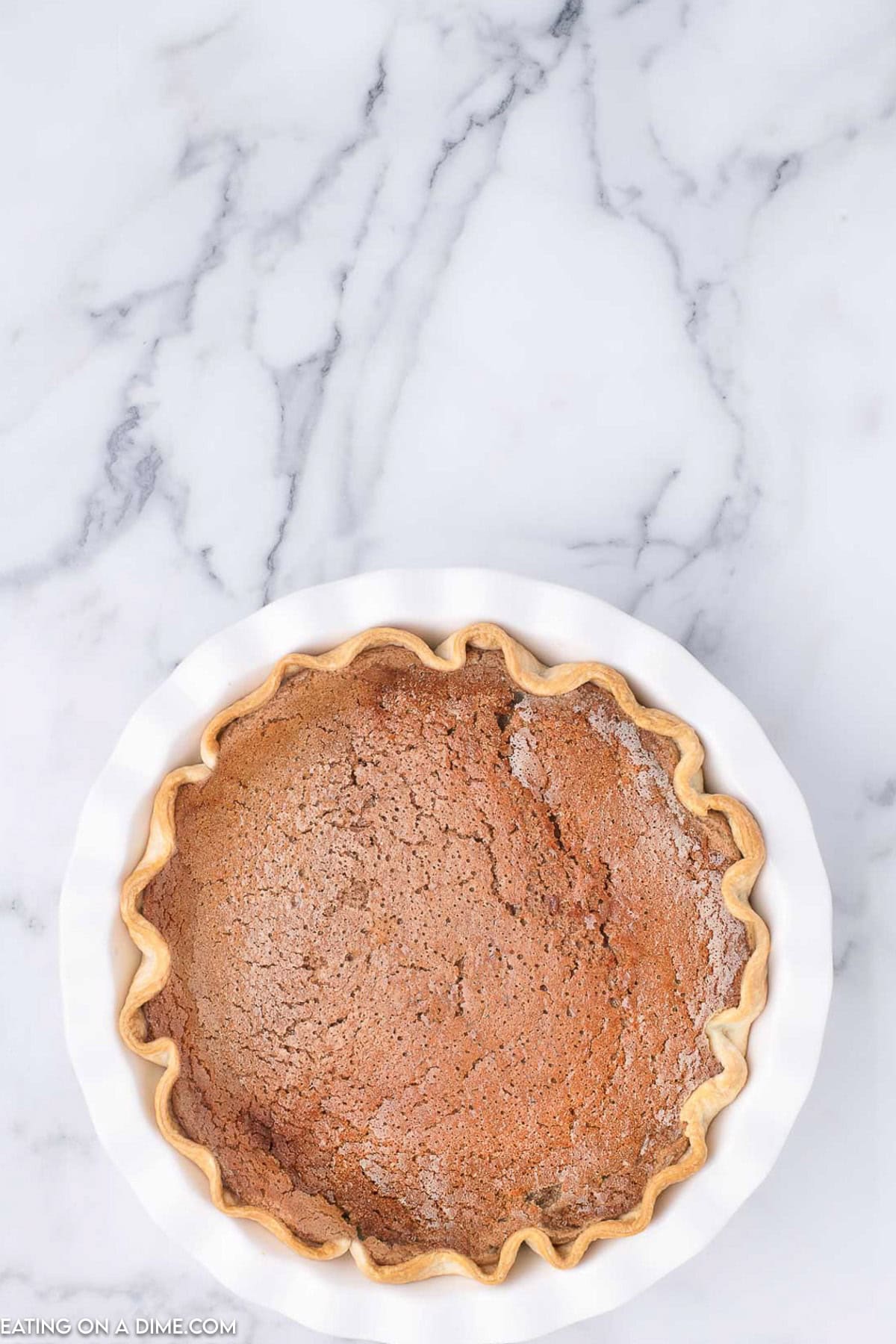 A freshly baked cinnamon chocolate pie with a fluted crust sits in a white pie dish on a marble countertop.