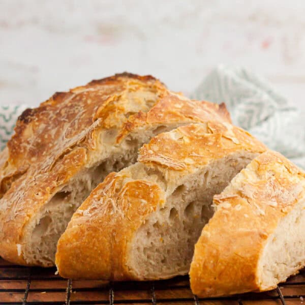 Close-up of freshly baked artisan bread from a cherished recipe, with a golden crust, sliced and resting on a cooling rack. The bread boasts a rustic appearance and airy texture inside, with a light patterned cloth in the background.