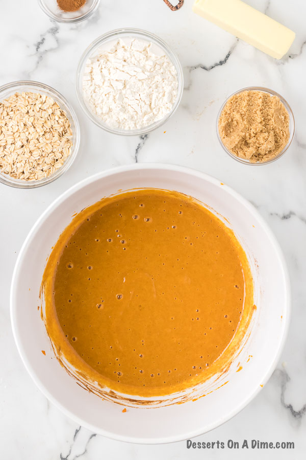 Pumpkin batter in a bowl with small bowls of oats, flour and brown sugar on the side with a stick of butter