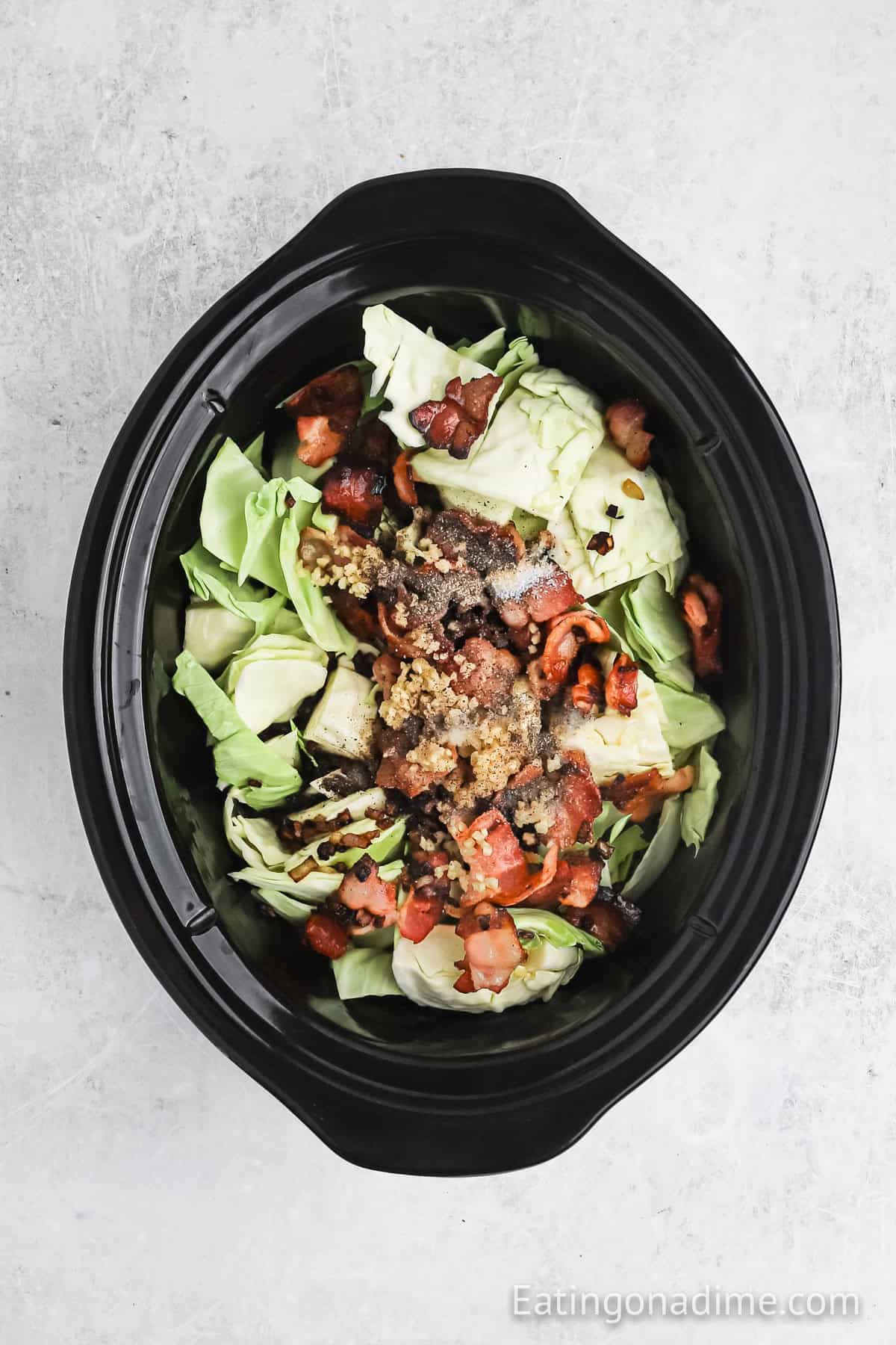 A slow cooker cabbage dish filled with chopped cabbage, bacon bits, and ground meat, all seasoned to perfection. The ingredients are uncooked, awaiting their slow-cooked transformation.