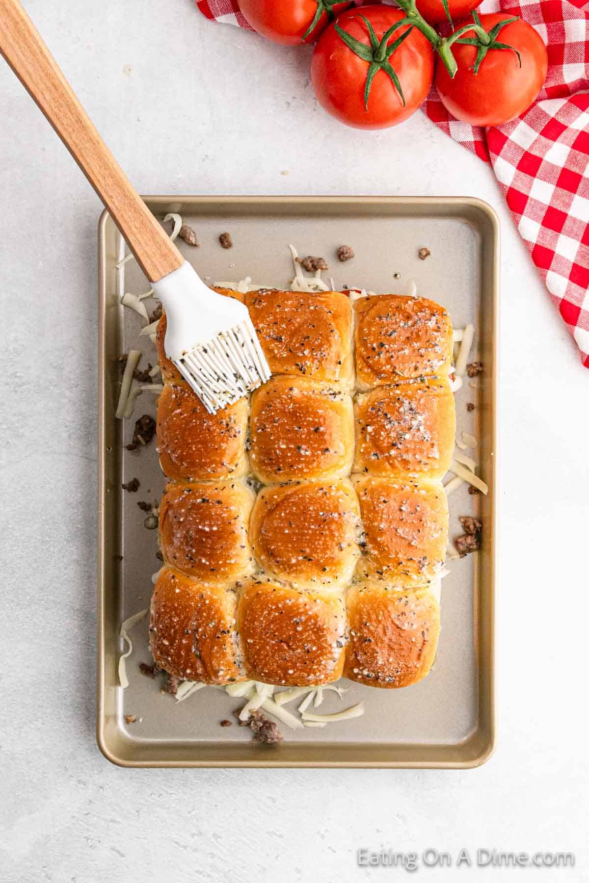 Brushing the melted butter over the buns on a baking sheet