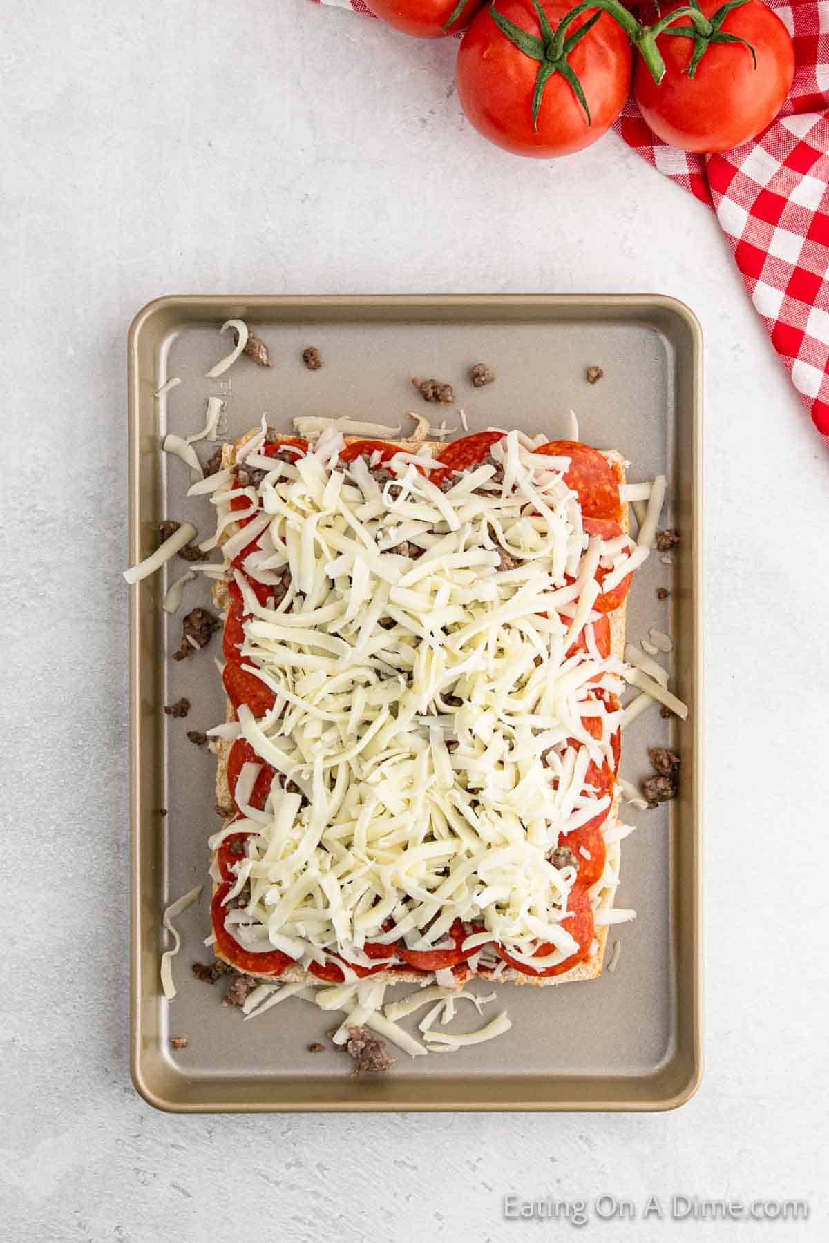 Shredded cheese on pepperoni on a baking sheet