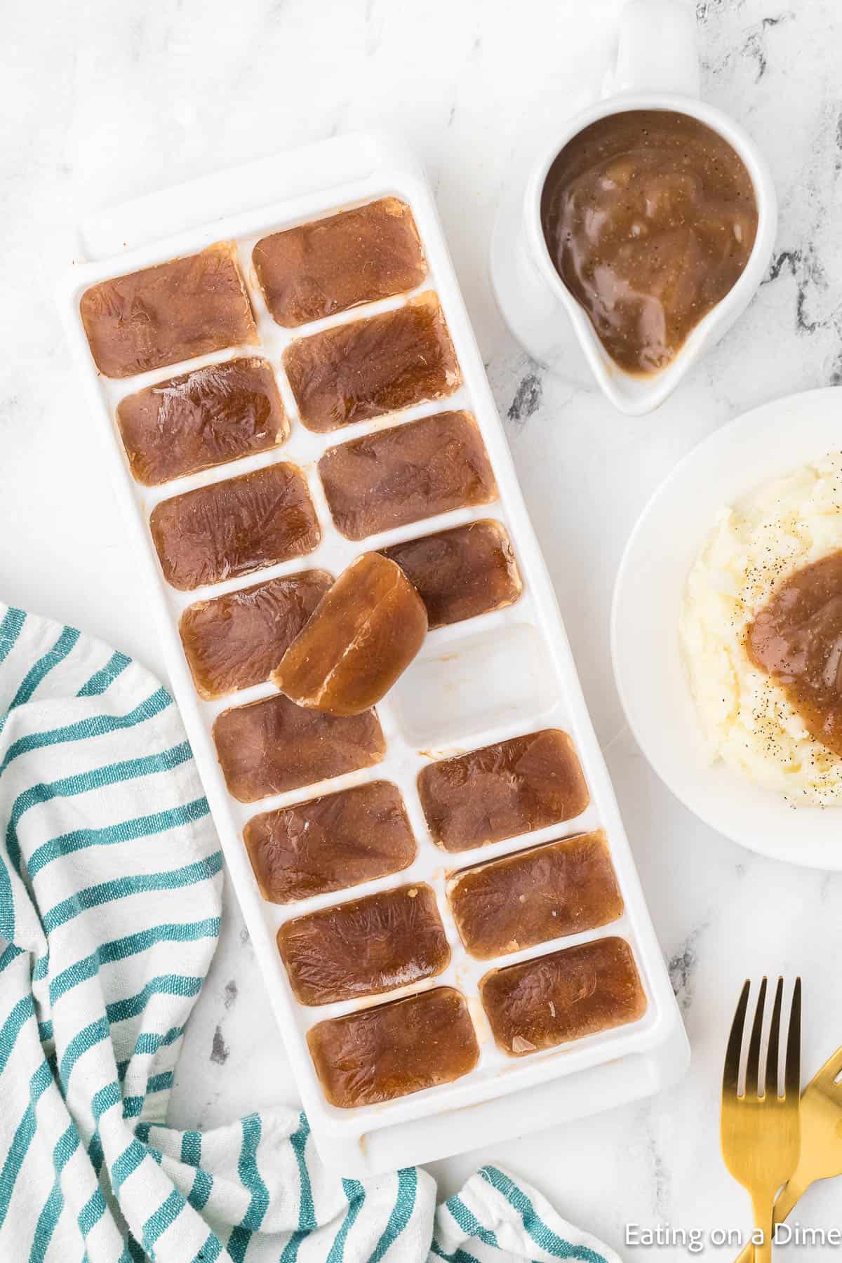 Ice tray with frozen gravy with a gravy boat full of gravy and a plate of mashed potatoes topped with gravy