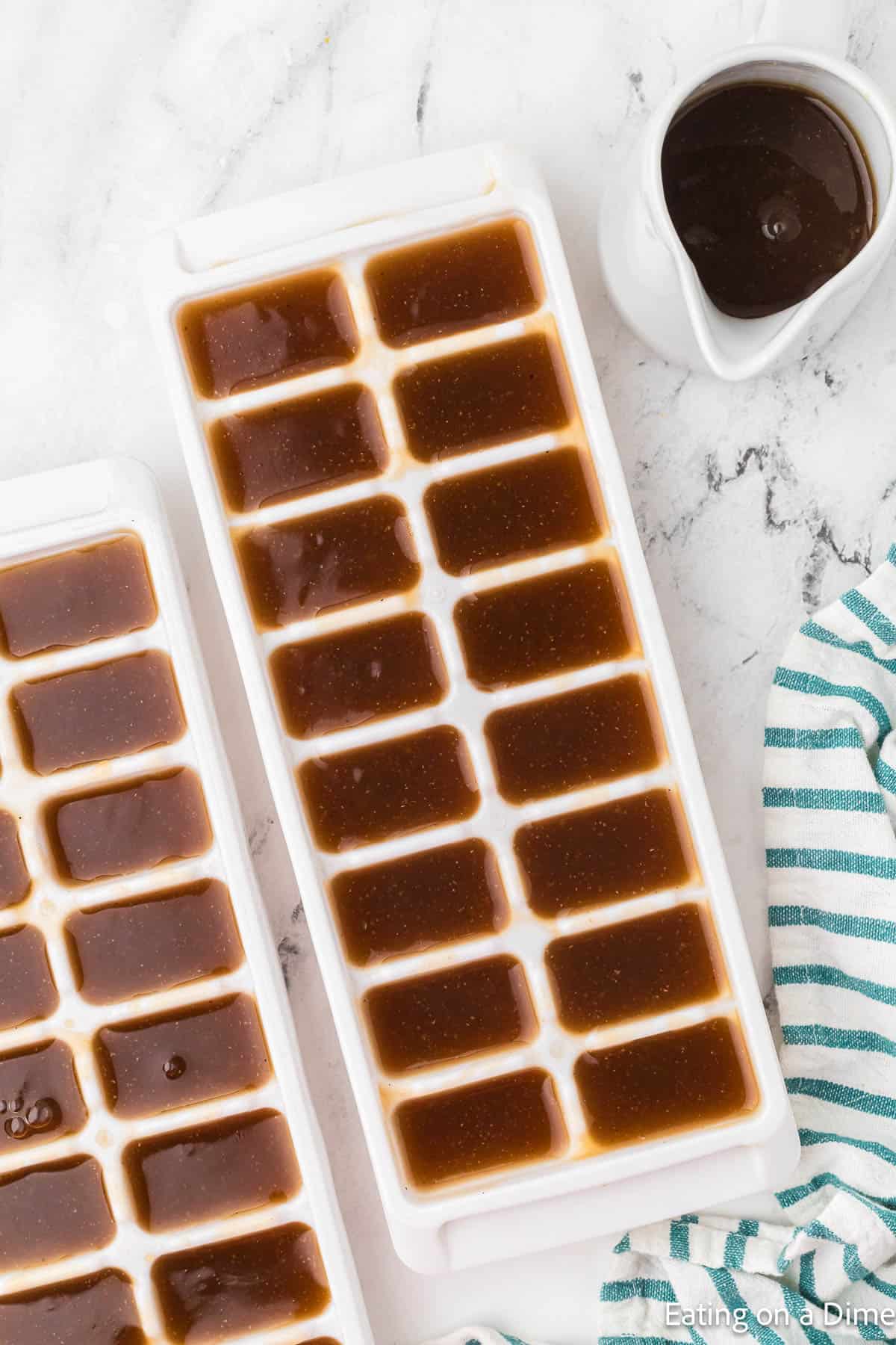 Ice cube trays full of gravy with a gravy boat of gravy