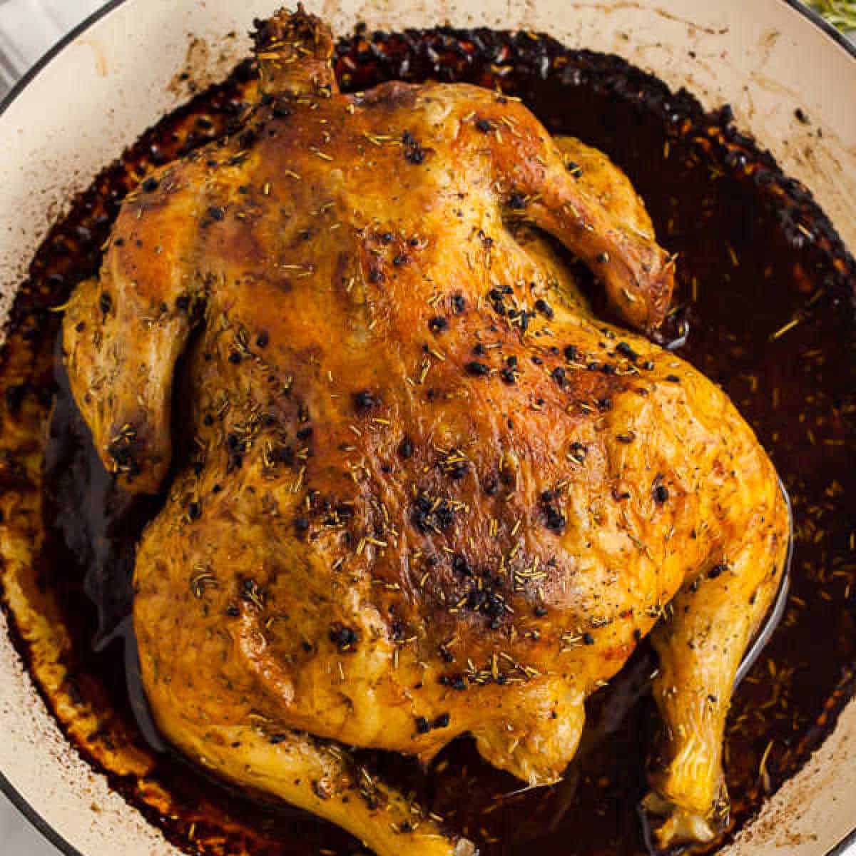 Discover how to roast a chicken with a golden-brown, crispy skin, seasoned with herbs. It rests in a dark, flavorful sauce in a round baking dish, offering an irresistible aroma and tenderness that will delight your senses.