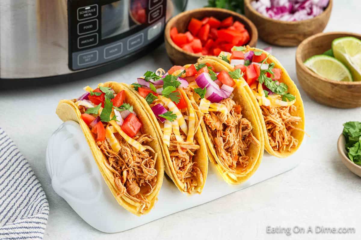 Chicken tacos in a taco stand with small bowls of diced tomatoes, red onions, fresh lime and cilantro on the side