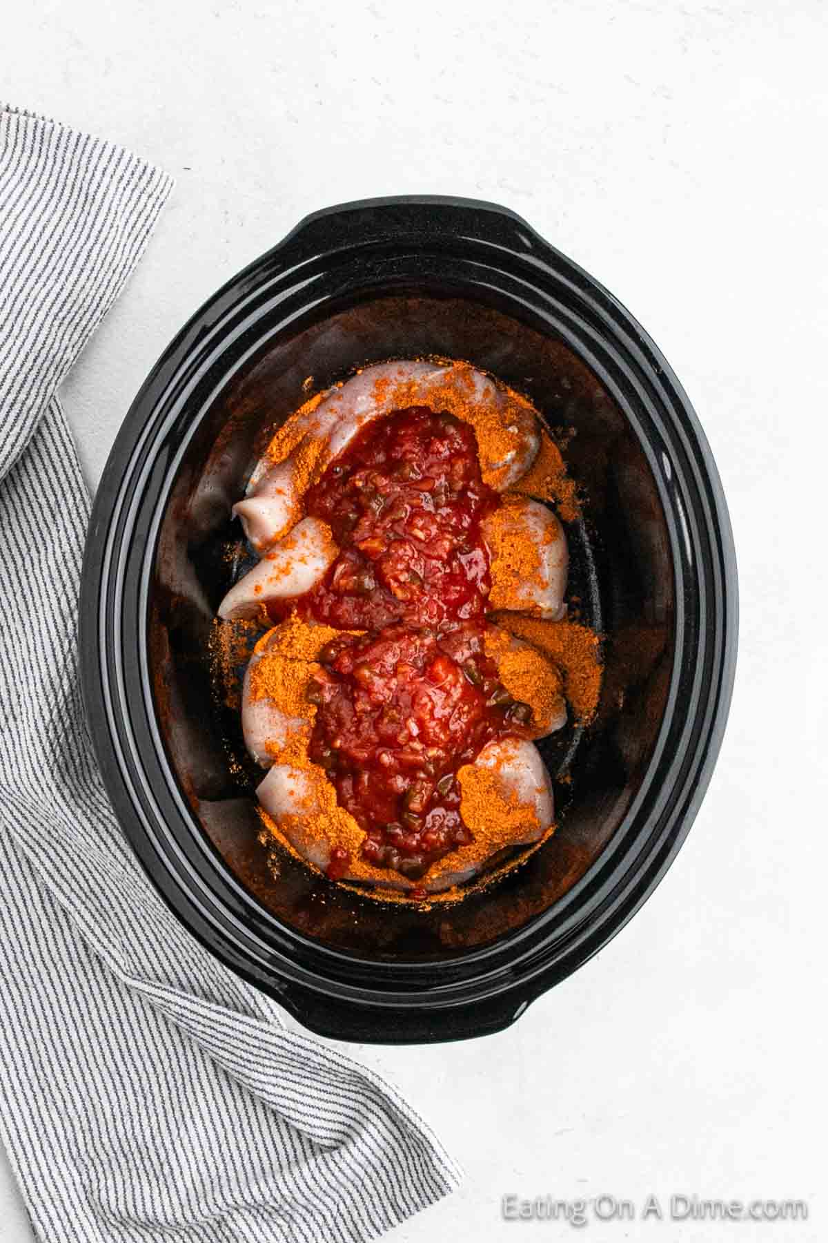 Salsa and taco seasoning spread over the chicken breast in the slow cooker