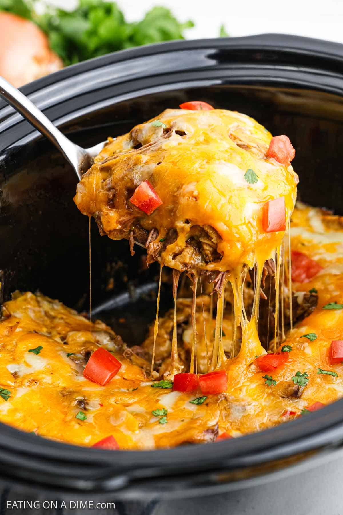 Shredded beef enchiladas topped with melted cheese and diced tomatoes with a serving on a spatula