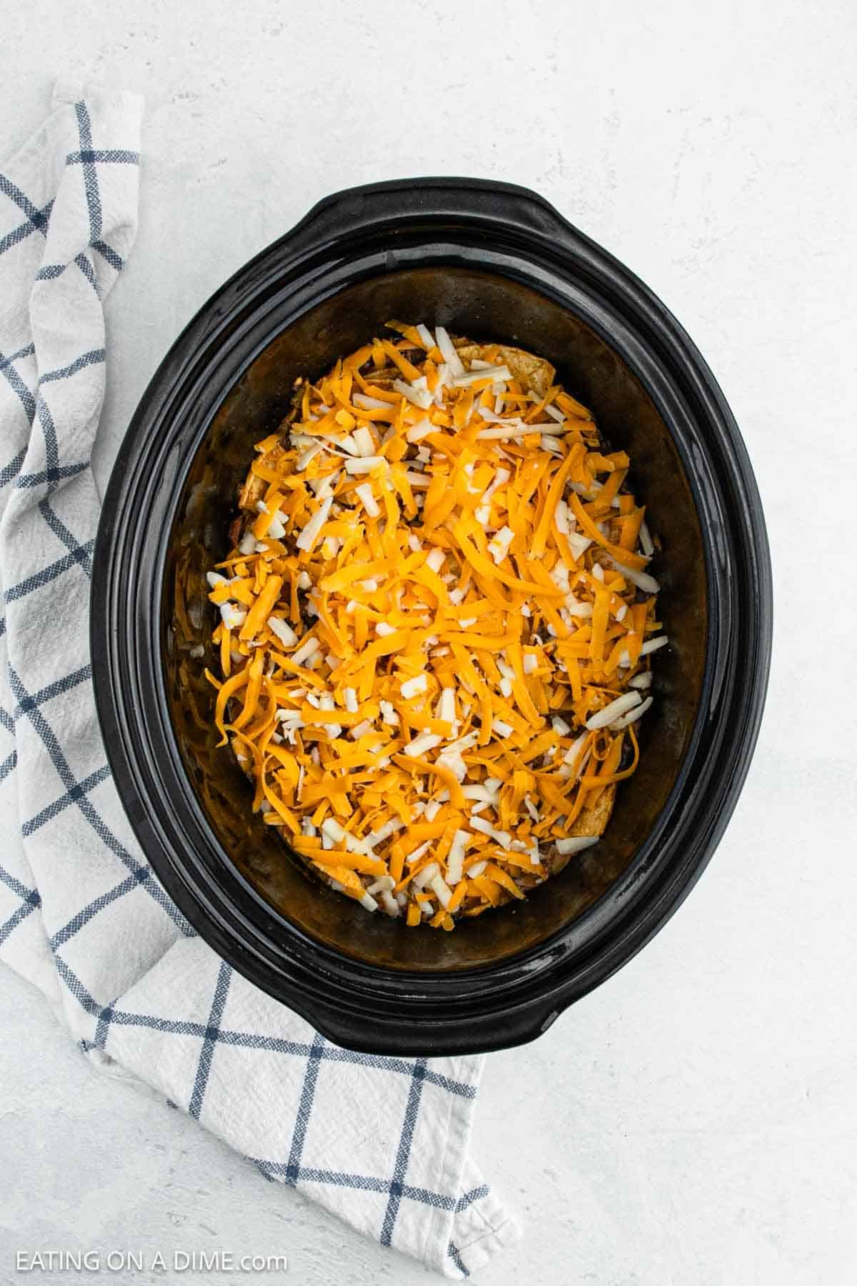 Shredded cheese on top of the beef enchiladas ingredients in the slow cooker