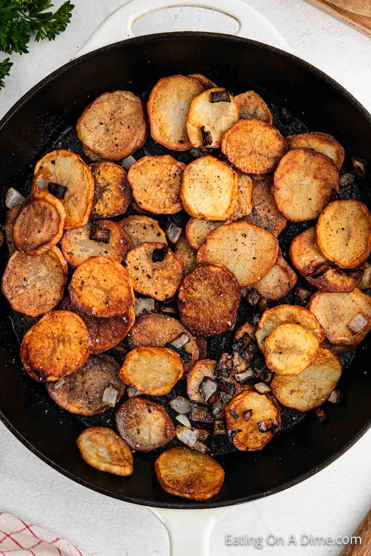 A skillet filled with slices of golden brown, pan-fried potatoes mixed with small pieces of cooked onions. The potatoes are round and crispy, and the onions are lightly charred, adding texture to the dish.