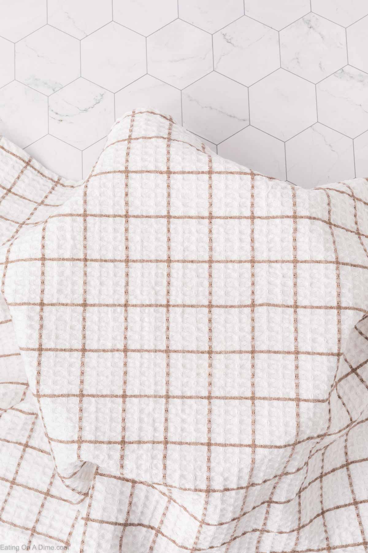 A textured white cloth with a grid pattern of thin brown lines is spread out on a surface with a white hexagonal tile design, reminiscent of the delicate lattice found atop freshly baked Mexican sweet bread.