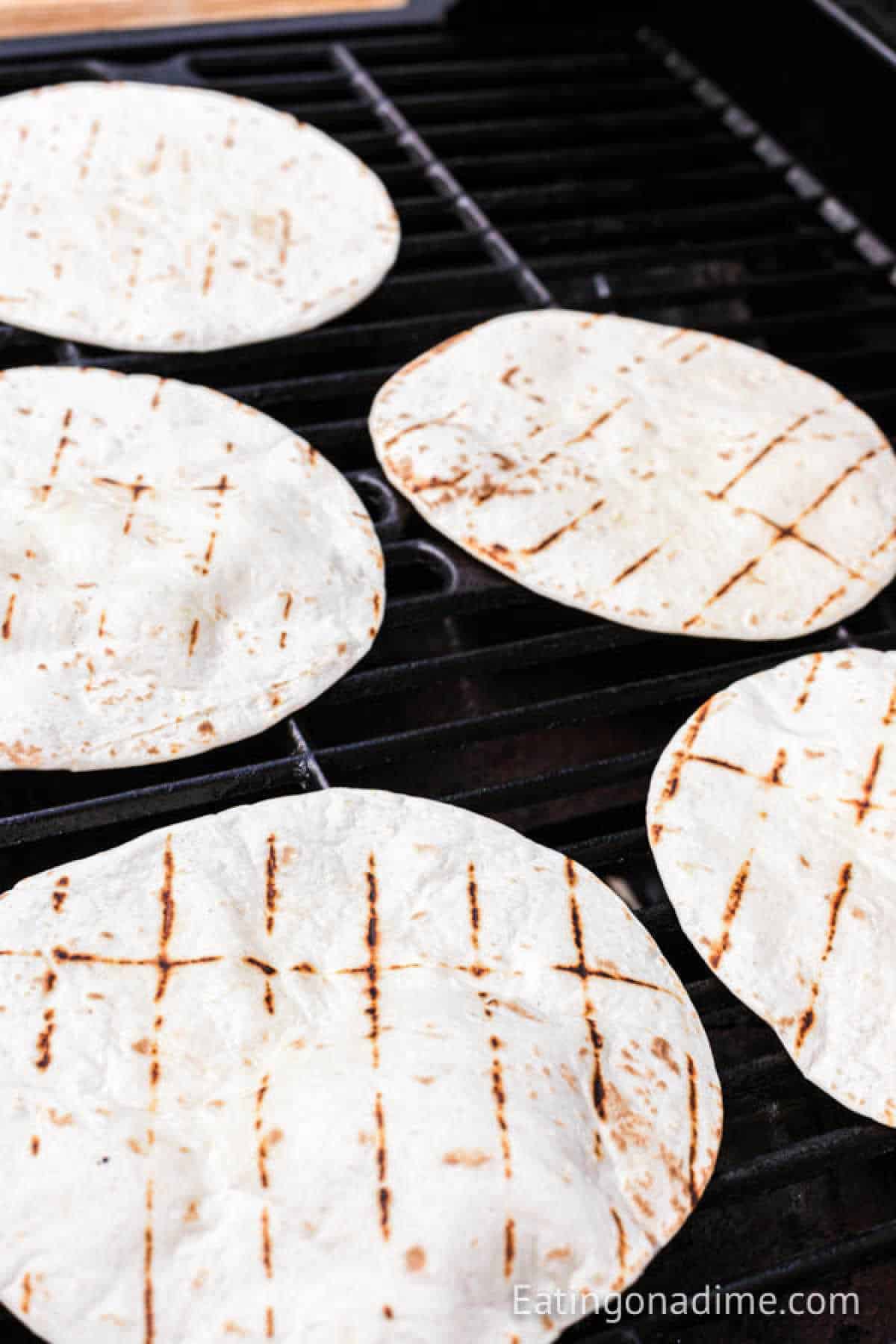 Grilled chicken fajitas sizzling on a black grill grate, their juicy flavors mingling with flour tortillas, each boasting perfect grill marks and a hint of browning.