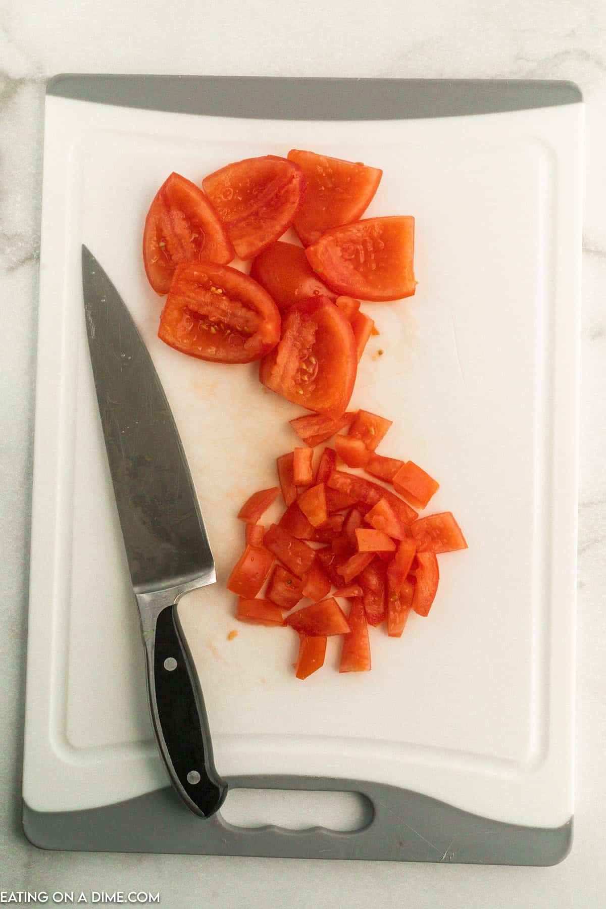 Dice tomato on a cutting board with a knife