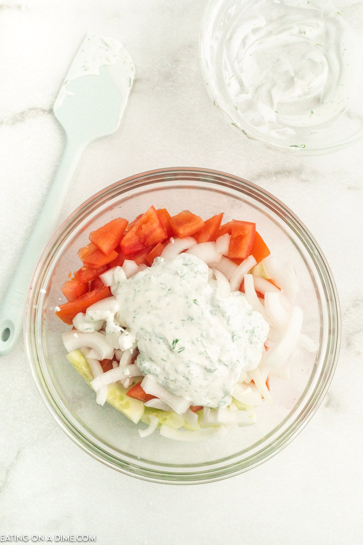 Pouring creamy sauce over diced onions, tomatoes and cucumber in a bowl