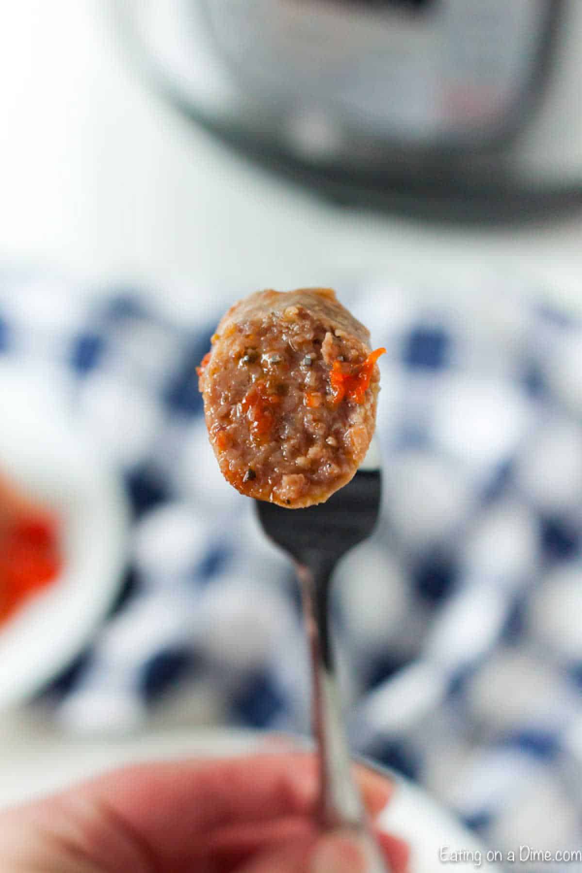 A close-up of a fork holding a savory meatball with a vibrant piece of red pepper, hinting at the delicious flavors of our Instant Pot Sausage and Peppers recipe. In the background, a blurred checkered cloth adds warmth to the scene.