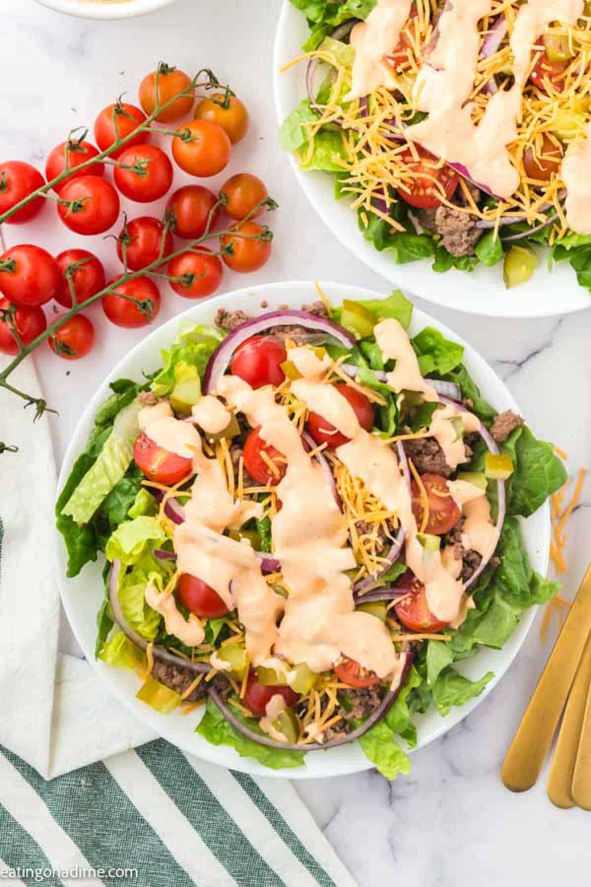 big mac salad topped with slice red onions, shredded cheese cherry tomatoes and drizzled with salad dressing