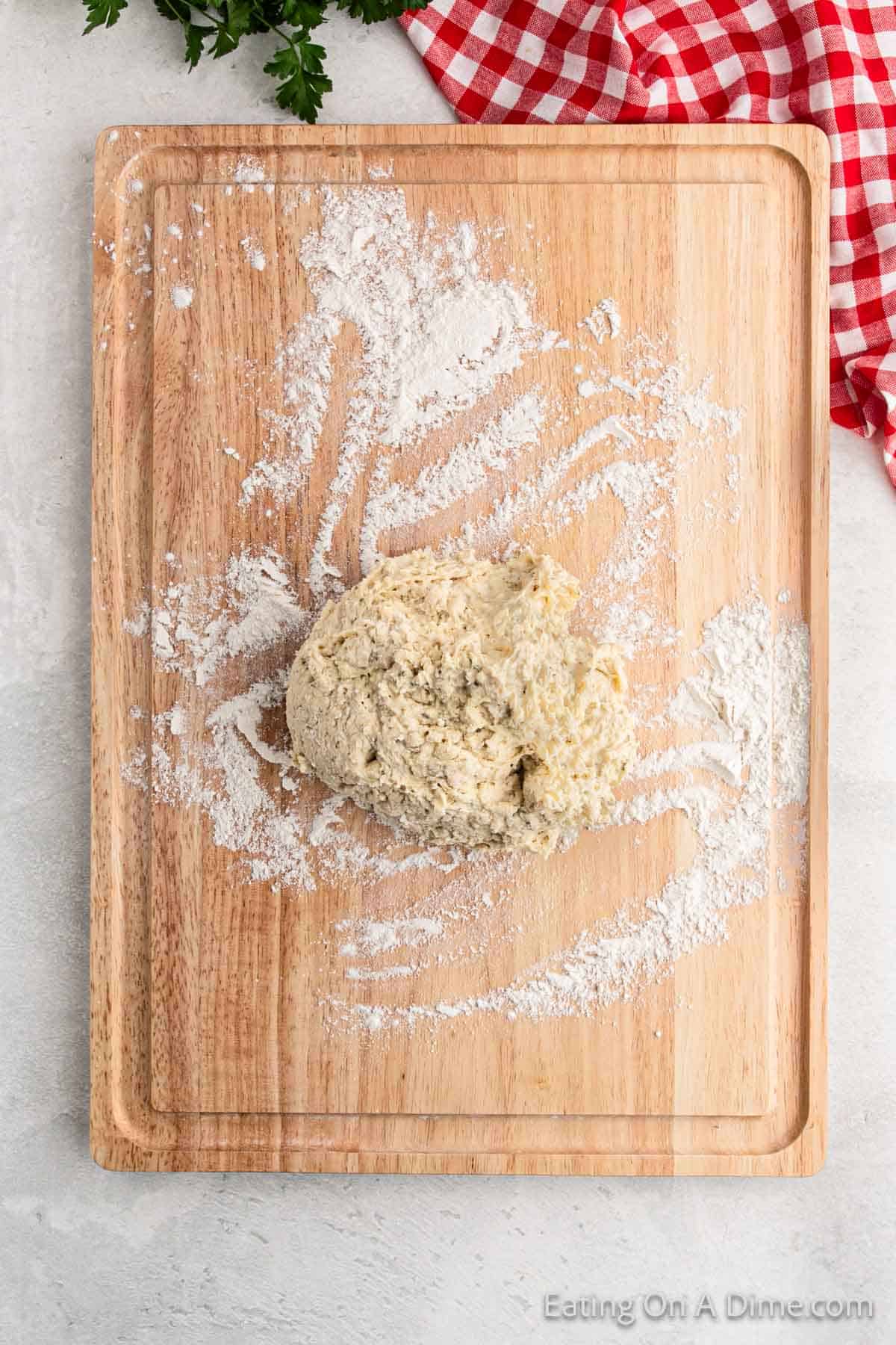 A wooden cutting board hosts a ball of dough in the center, surrounded by scattered flour, hinting at a delightful pizza pocket recipe. A red and white checkered cloth peeks into view at the top right corner.