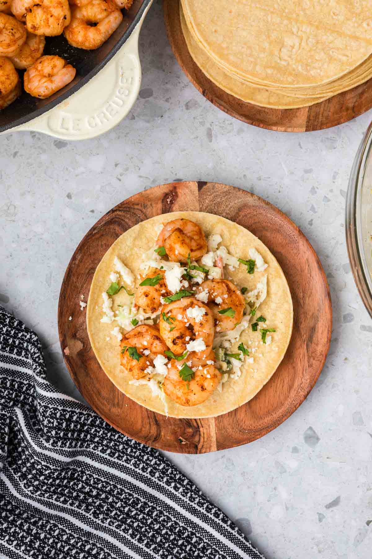 corn tortillas on a wooden platter topped with cooked shrimp, cilantro and cojita cheese