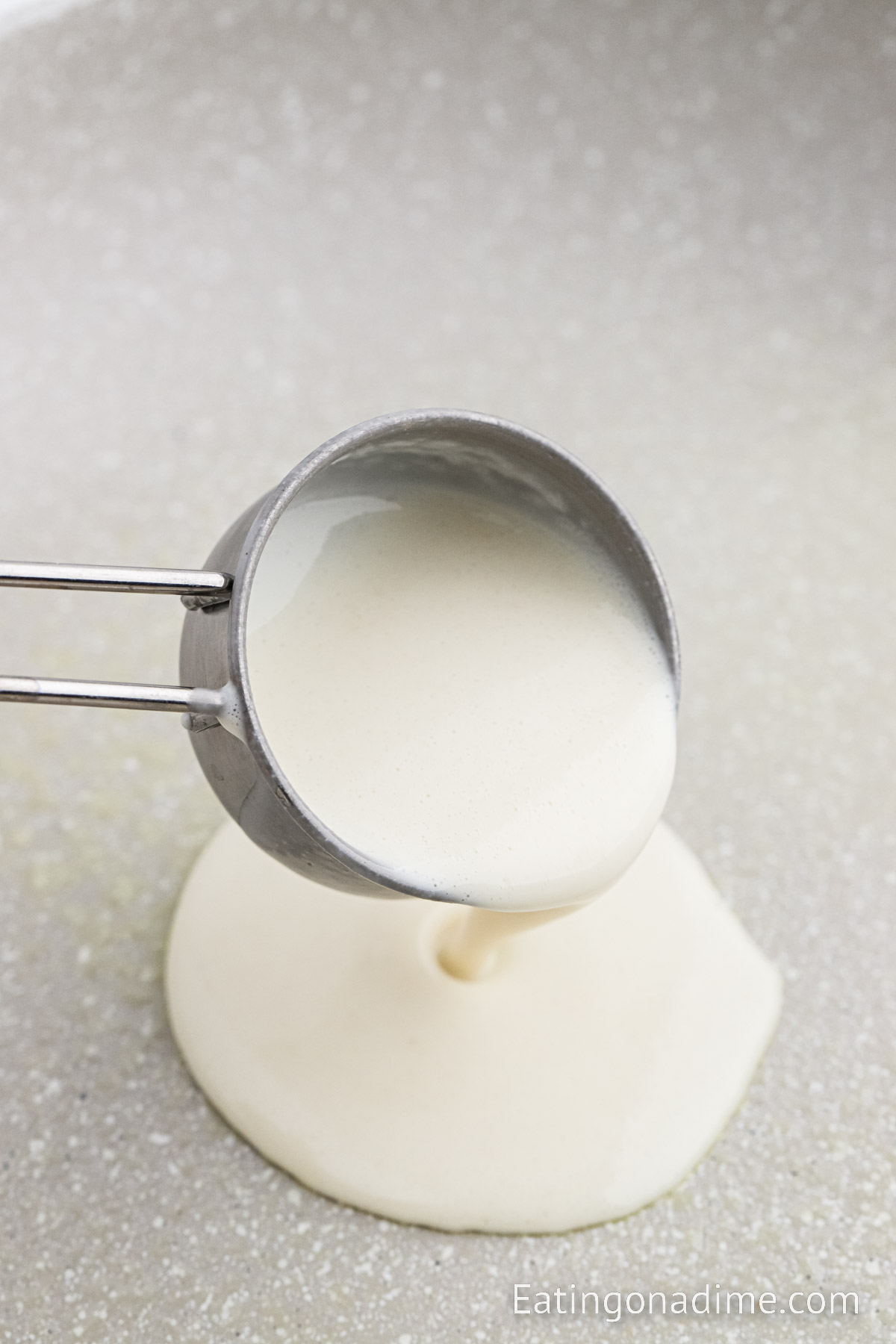 Pouring crepe batter in skillet with a measuring cup