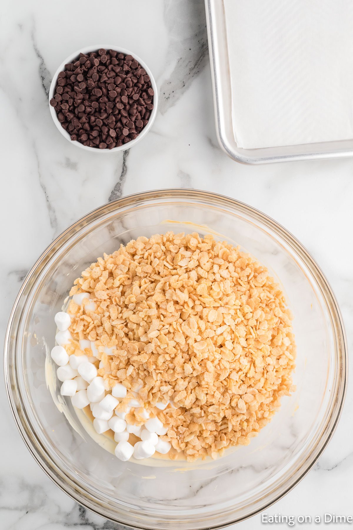 A small bowl of chocolate chips with a large bowl of crispy cereal and marshmallows