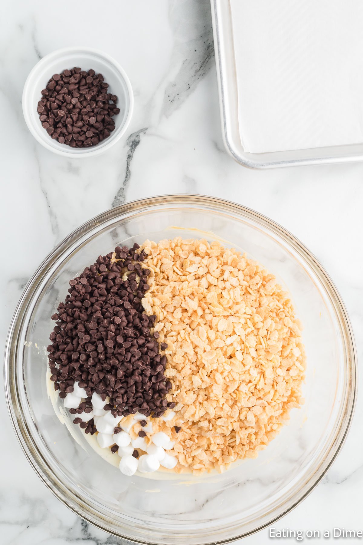 Small bowl of chocolate chips and a larger bowl of chocolate chips and crispy cereal and marshmallows