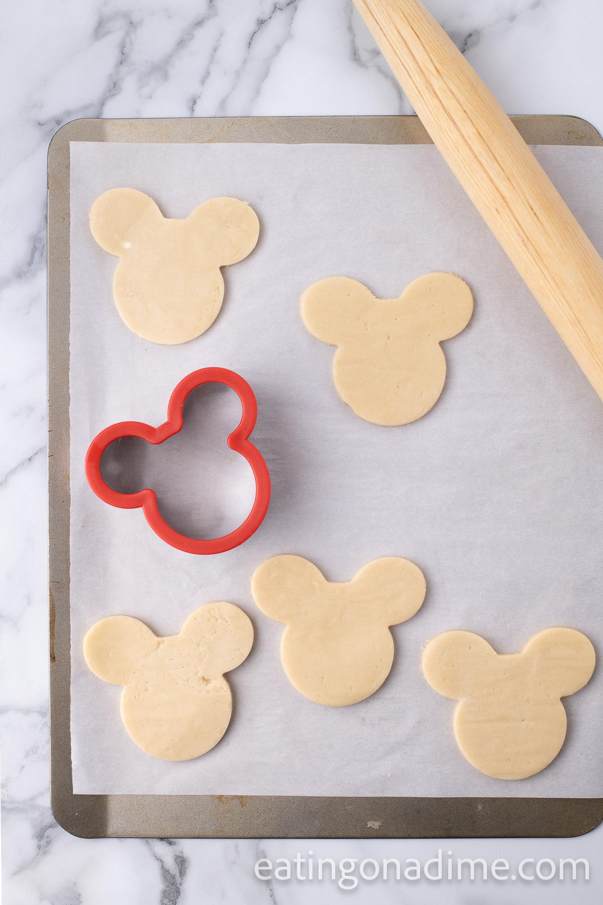 Mickey Mouse cut out cookie dough on a baking sheet lined with parchment paper and a rolling pin