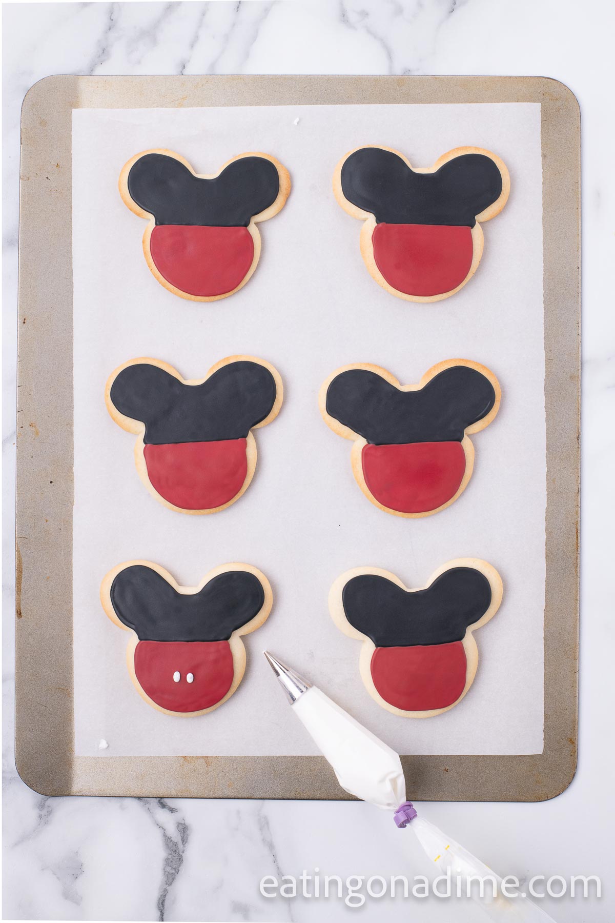 Mickey Mouse cookies decorated with black and red icing on a baking sheet lined with parchment paper