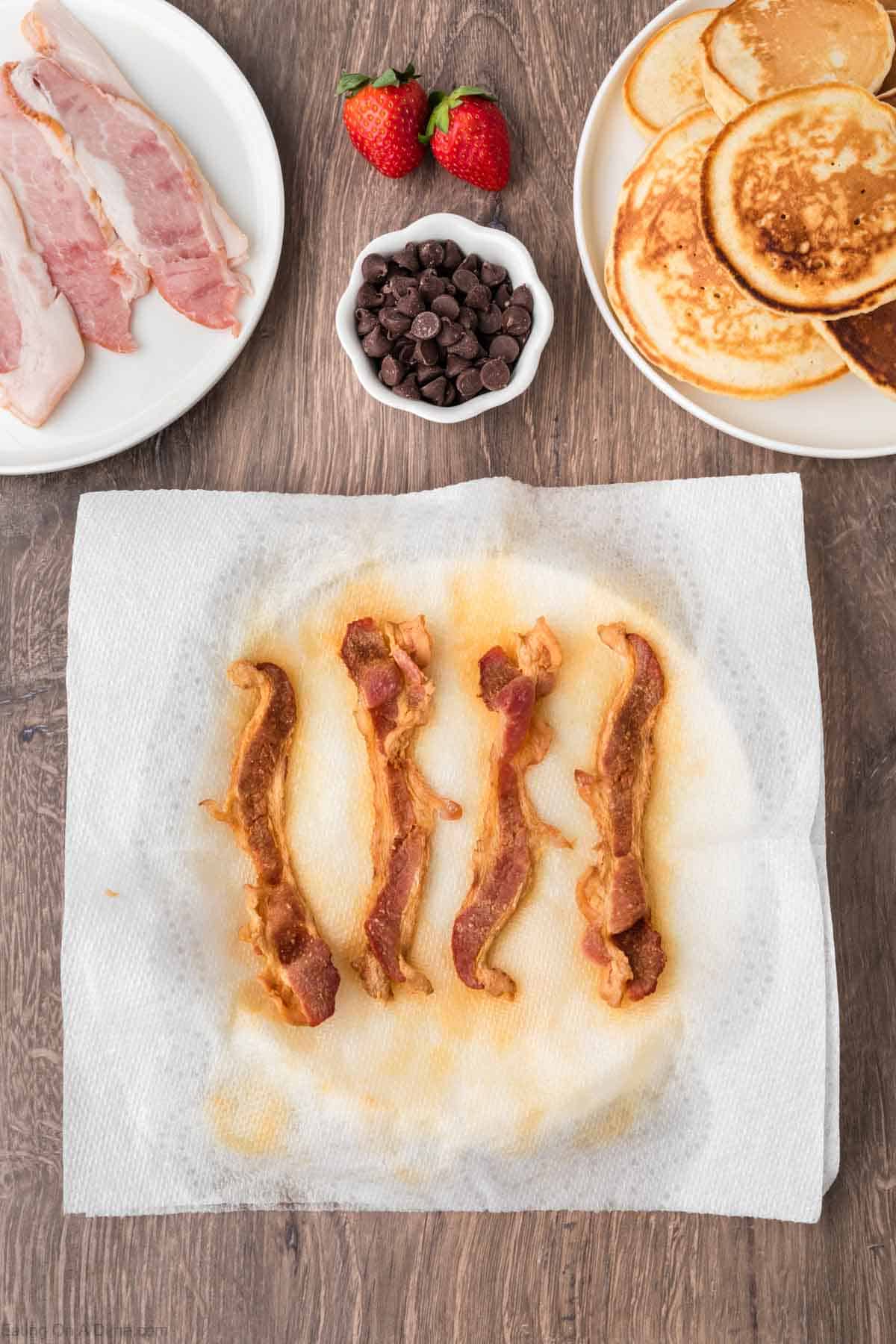 Cooked bacon on a plate with a plate of pancakes stacked  on the side