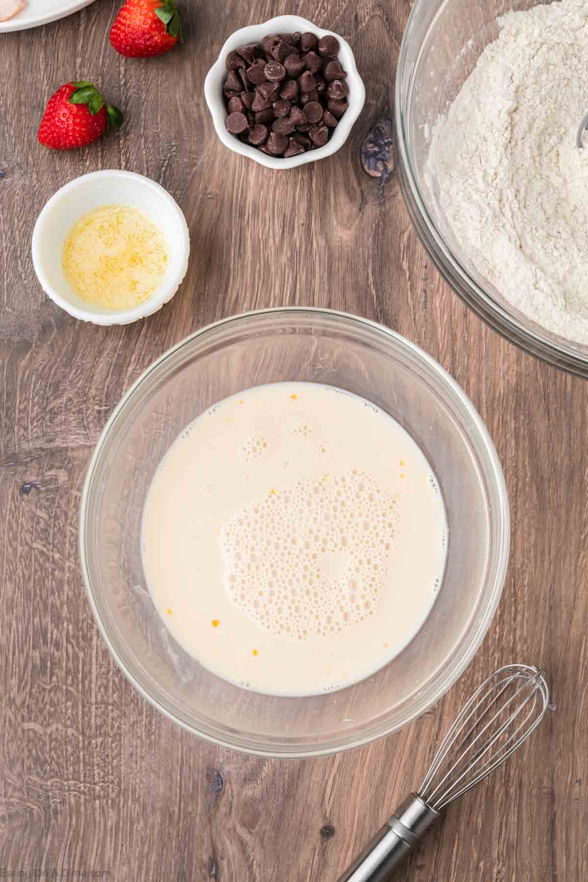 Egg, milk and vanilla in a bowl with small bowls of melted butter and chocolate chips